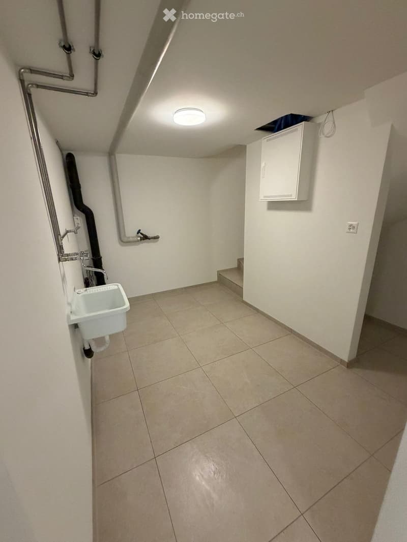 Empty hallway with tiled floor, white walls, a small sink on the left, and a white cabinet on the right. A small staircase leads upwards.