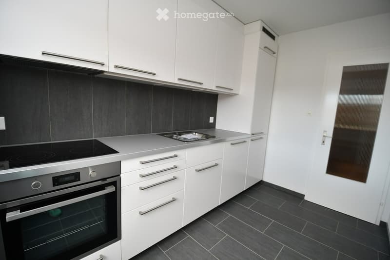 Modern kitchen with white cabinets, stainless steel appliances, induction cooktop, and dark tiled floor.