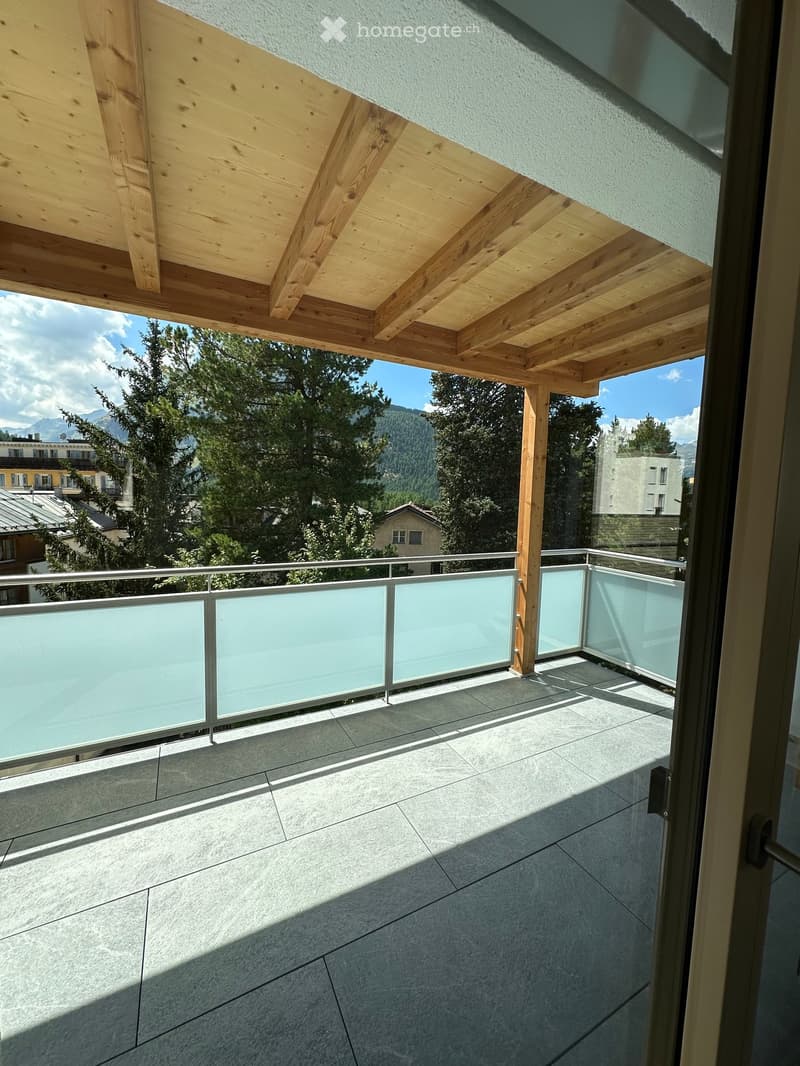 Balcony with wooden ceiling, glass railing, and tiled floor, overlooking a scenic mountain view.