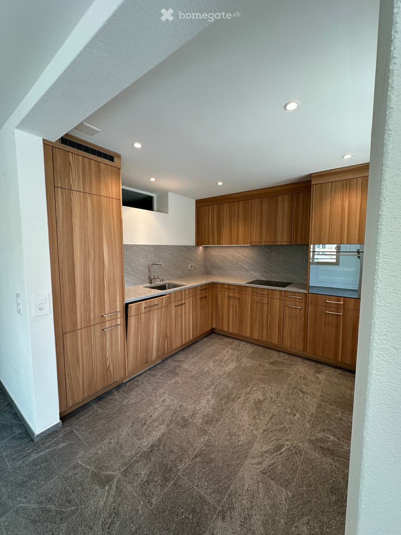 Modern kitchen with wooden cabinets, stainless steel sink, and stove, featuring recessed lighting and tiled flooring.