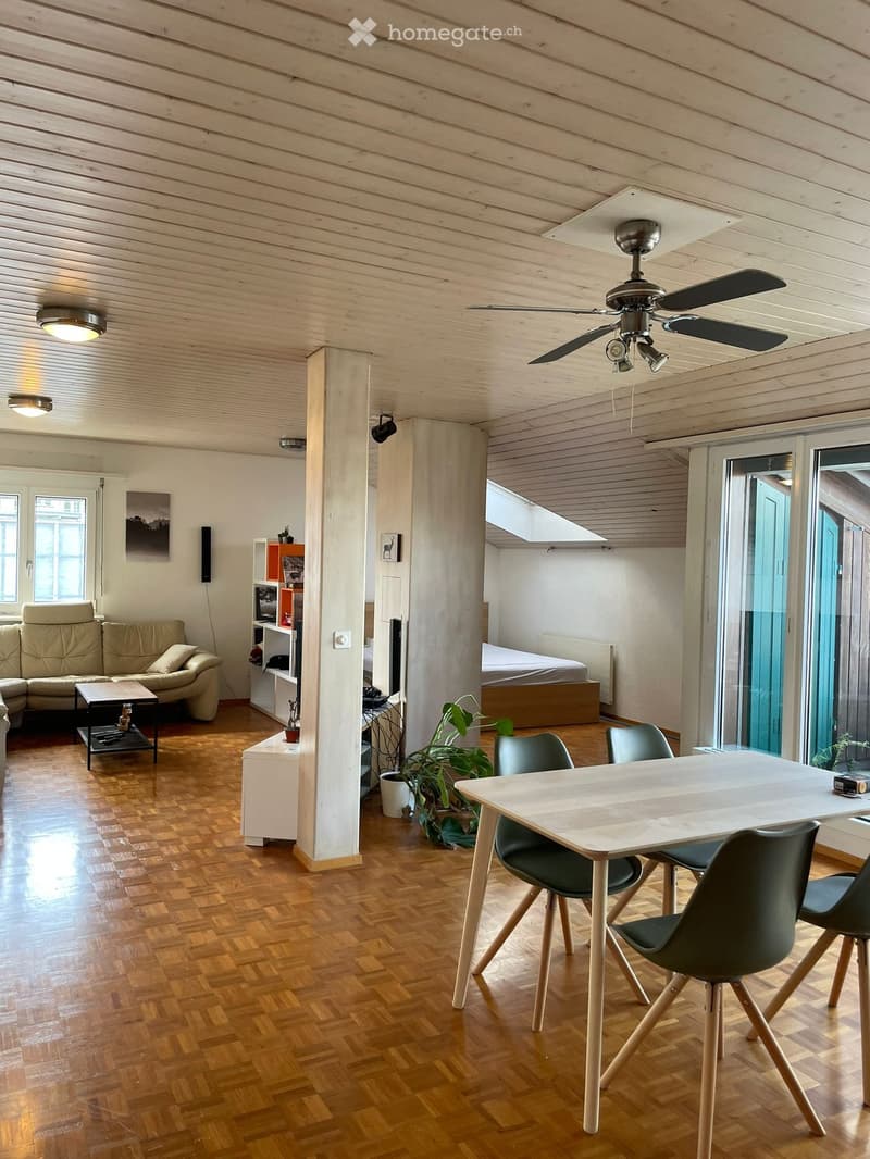 Open-plan living and dining area with wooden flooring, a sofa, coffee table, dining table with chairs, and a ceiling fan.