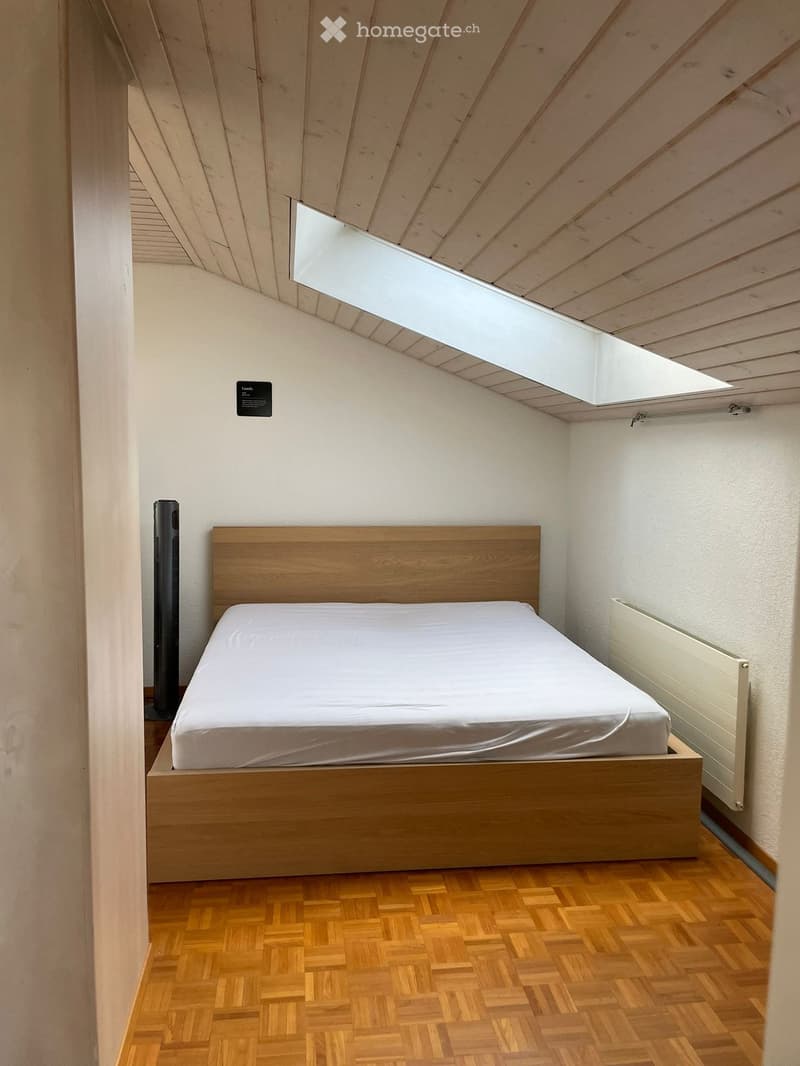 Modern bedroom with a wooden bed, white bedding, herringbone wooden flooring, and a radiator on the wall.