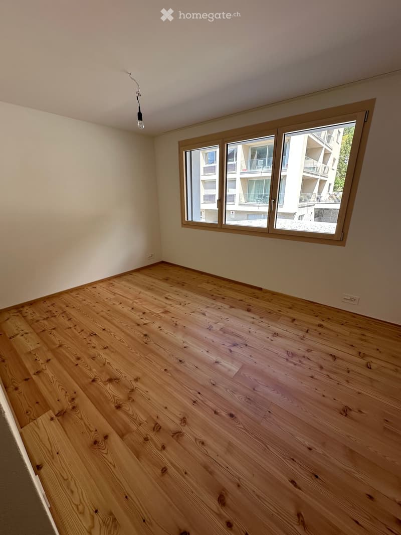 Empty room with wooden flooring, large window, and visible light fixture on the ceiling.