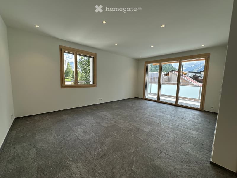 Empty room with grey tiled floor, light green walls, and large windows offering a scenic mountain view. The room features recessed lighting and a sliding glass door leading to a balcony.