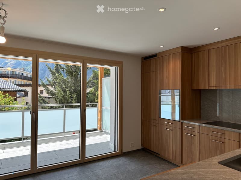 Modern kitchen with wooden cabinets, stainless steel oven, and large sliding glass doors opening to a balcony with mountain view.