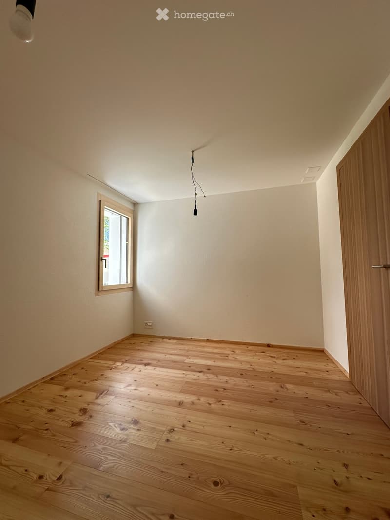Empty room with light wooden flooring, white walls, and a single window with a wooden frame. The room has a simple, clean design with no furniture or decorations.