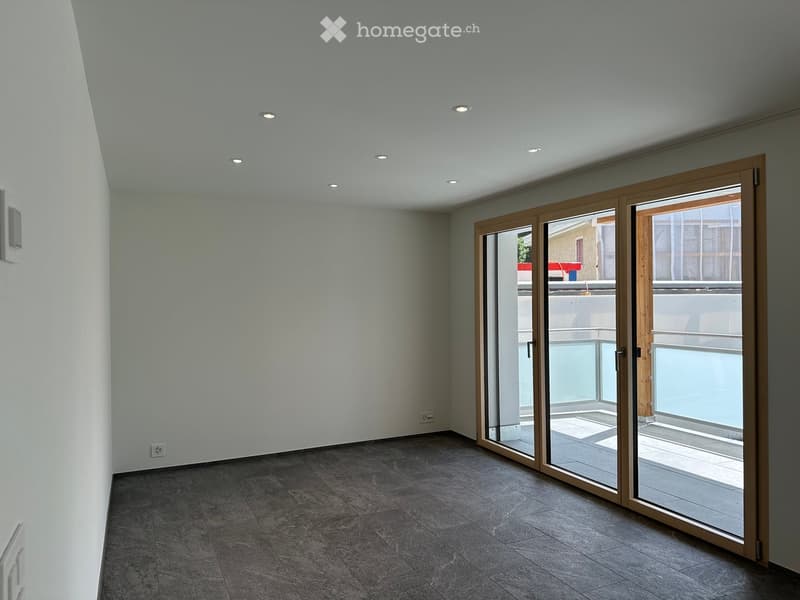 Empty room with grey tiled floor, white walls, recessed ceiling lights, and large sliding glass doors leading to a balcony.