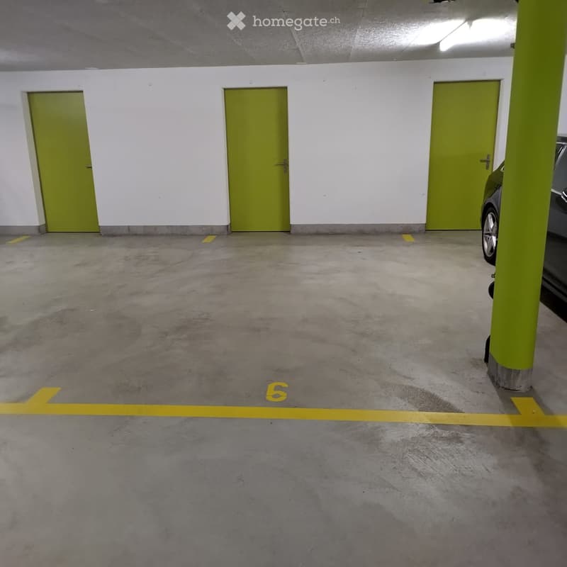 Underground parking area with concrete floors, white walls, green doors, and yellow parking lines.