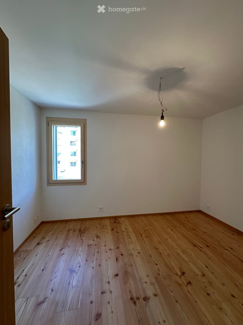 Empty room with wooden flooring, white walls, a single window, and a hanging light fixture.