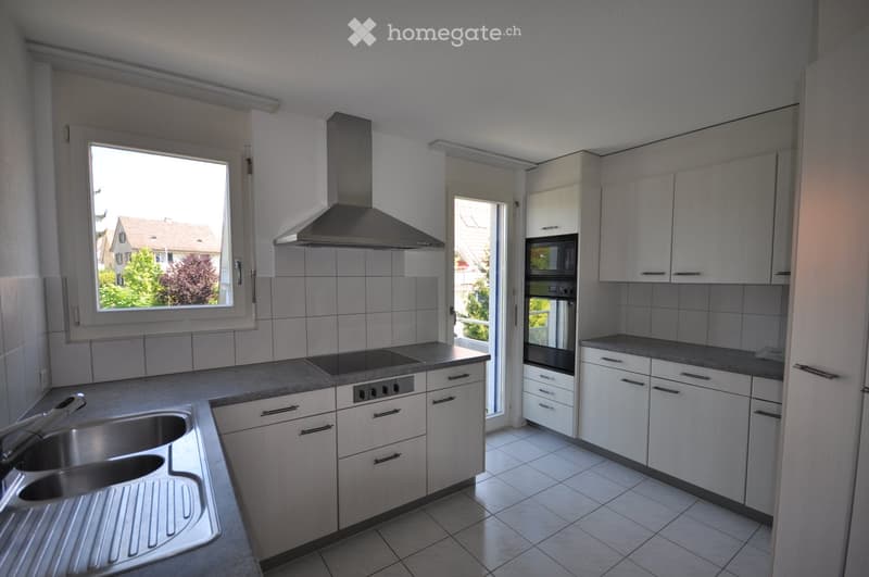 Modern kitchen with white cabinets, stainless steel appliances, and a large window overlooking a residential area.
