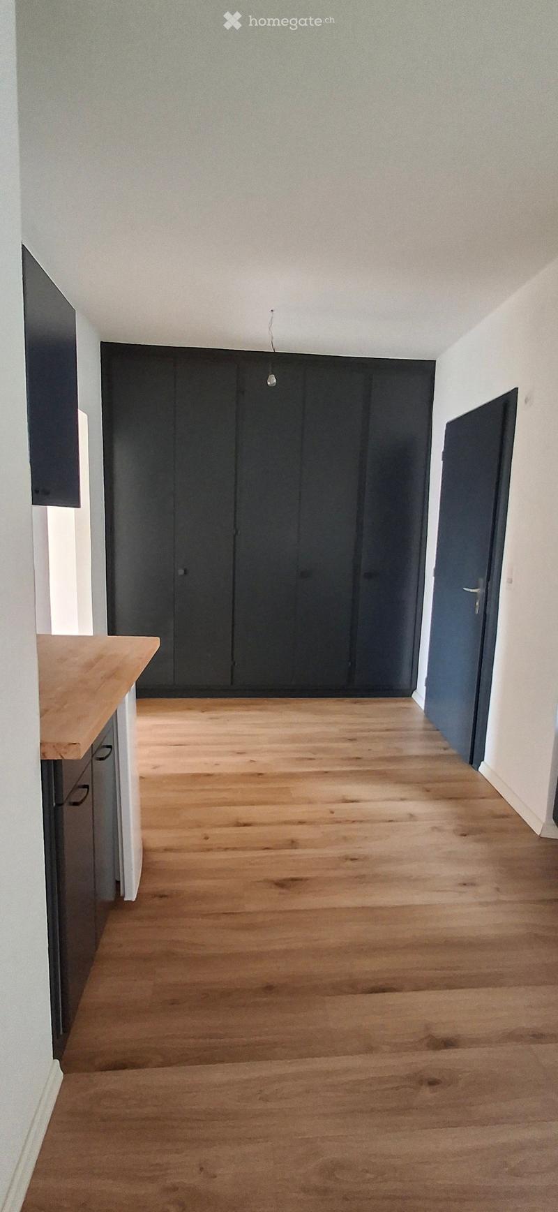 Empty room with wooden flooring, white walls, and dark cabinetry along one wall. No furniture or equipment present.