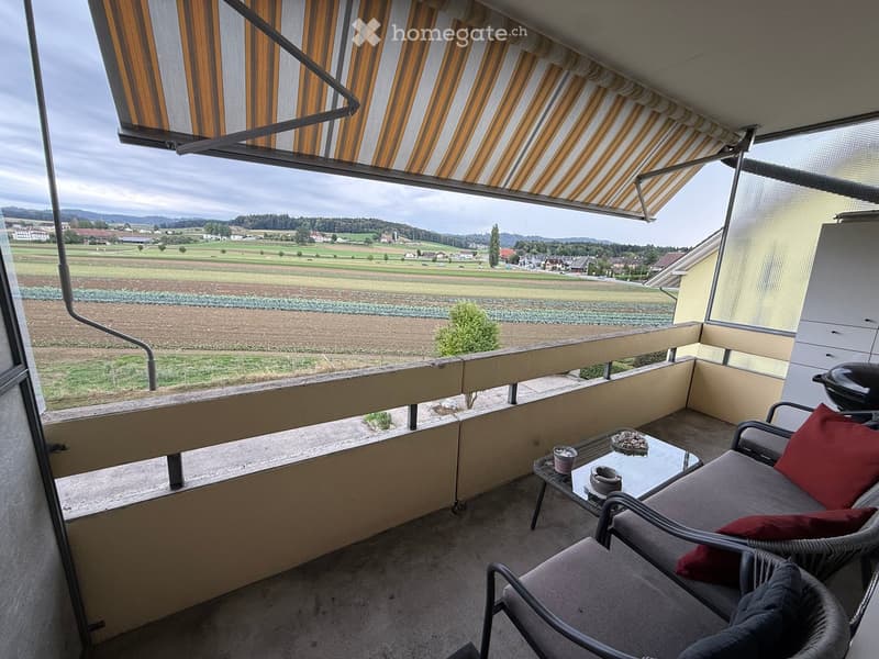Balcony with a view of a rural landscape, featuring a lounge chair, small table, and cups.