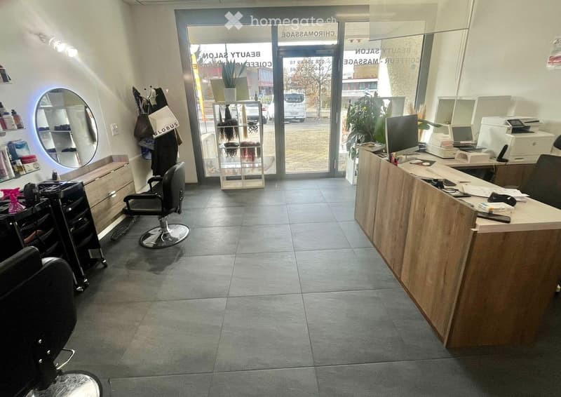 Modern reception area with a counter, chairs, a large mirror, shelves, and a plant near the entrance.