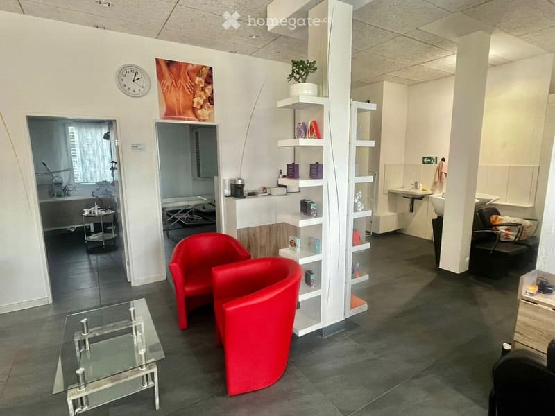 Modern, well-lit room with red chairs, a glass table, shelves, a sink, and a bathtub visible in the background.