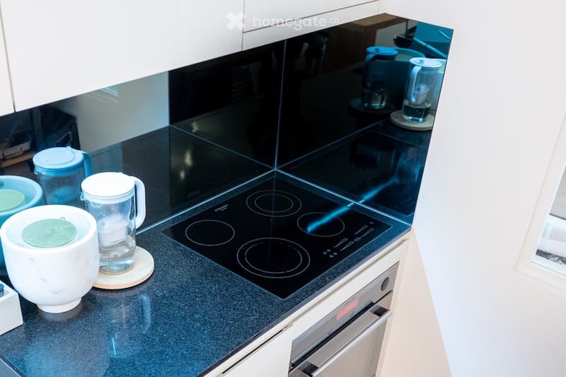 Modern kitchen with black induction cooktop, white cabinets, and various kitchen items including a blender, cups, and bowls on the countertop.