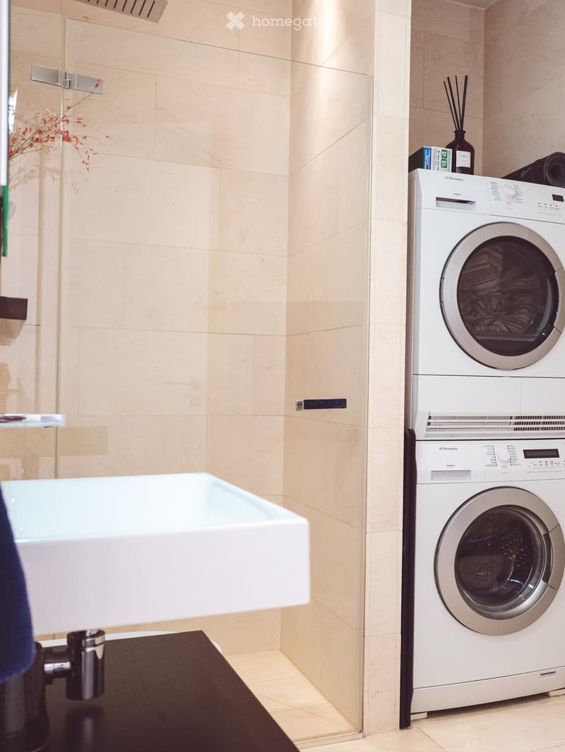 Modern bathroom with a white washing machine and dryer stacked, a white sink, and beige tiled walls.