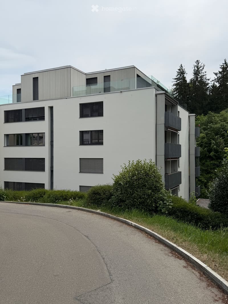 Modern two-story house with white facade, large windows, and balconies. The house features a sleek, contemporary design with a flat roof and glass railings on the upper level.