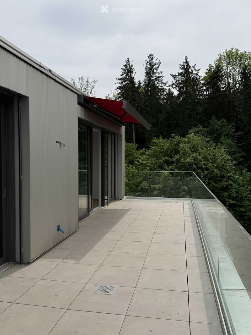 Modern balcony with a glass railing, tiled floor, and a red awning extending from the building.