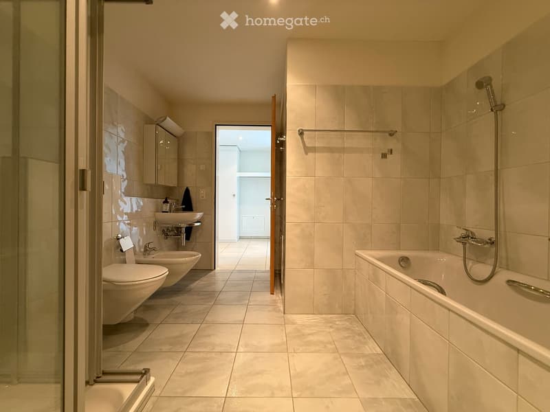 Modern bathroom with beige tiles, a bathtub, shower, toilet, sink, and a mirrored cabinet.