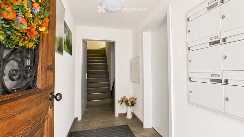 Hallway with a staircase leading upwards, mailboxes on the right, and a decorative wreath on the left door.