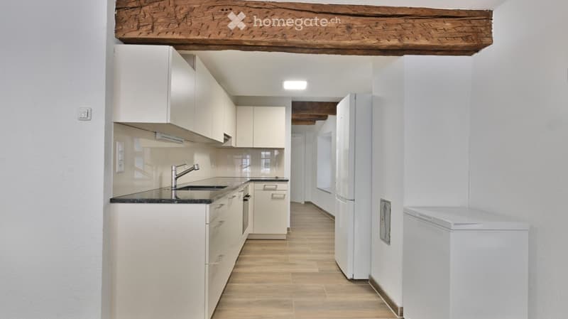 Modern kitchen with white cabinets, a stainless steel sink, and a refrigerator. The space features wooden flooring and exposed wooden beams on the ceiling.