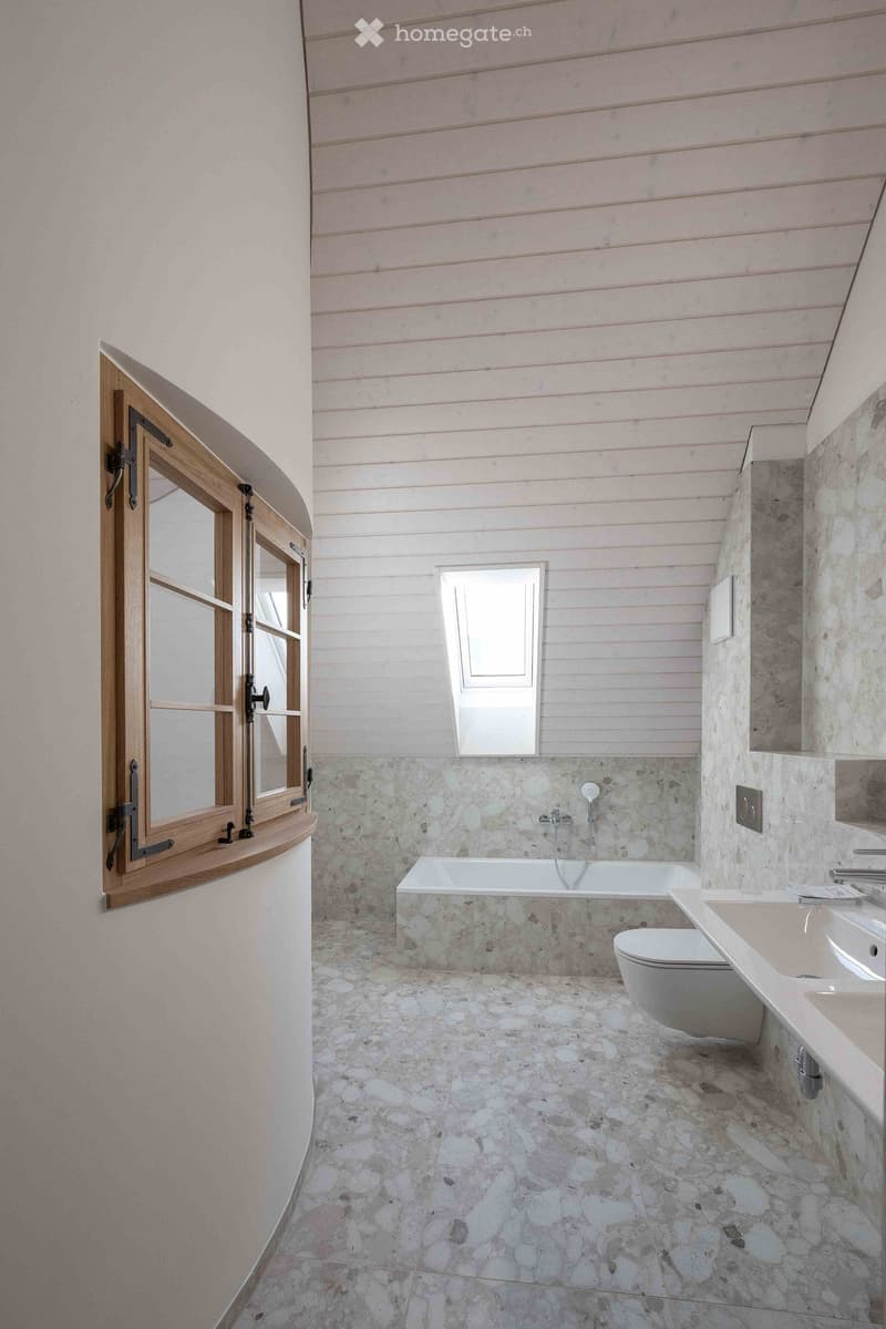 Bathroom with stone tiled walls and floor, a bathtub, toilet, sink, and a window with wooden frame.