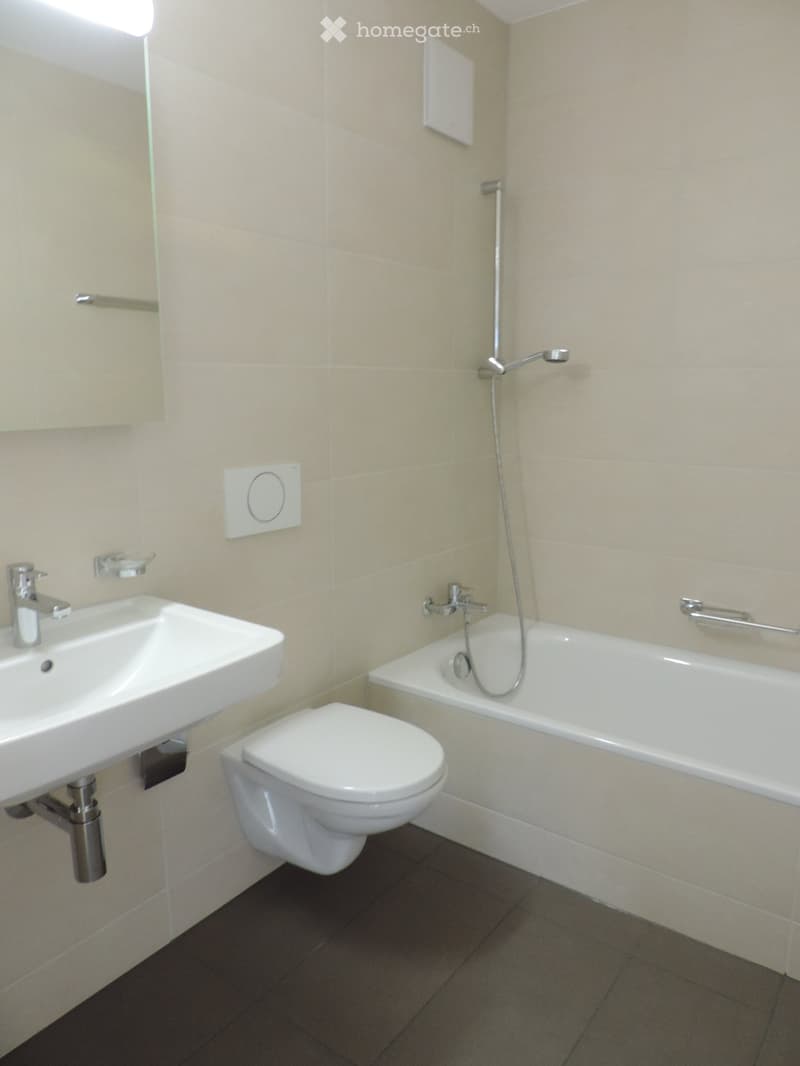 Modern bathroom with a white sink, toilet, bathtub, and chrome fixtures. Beige tiled walls and dark tiled floor.