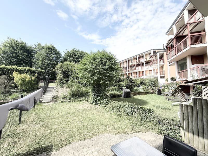 Garden / Outdoor Area. Garden area with grassy lawn, trees, and a multi-story building with balconies in the background.