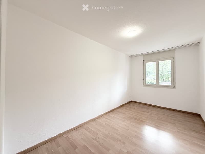 Empty room with white walls, wooden flooring, and a single window with blinds.