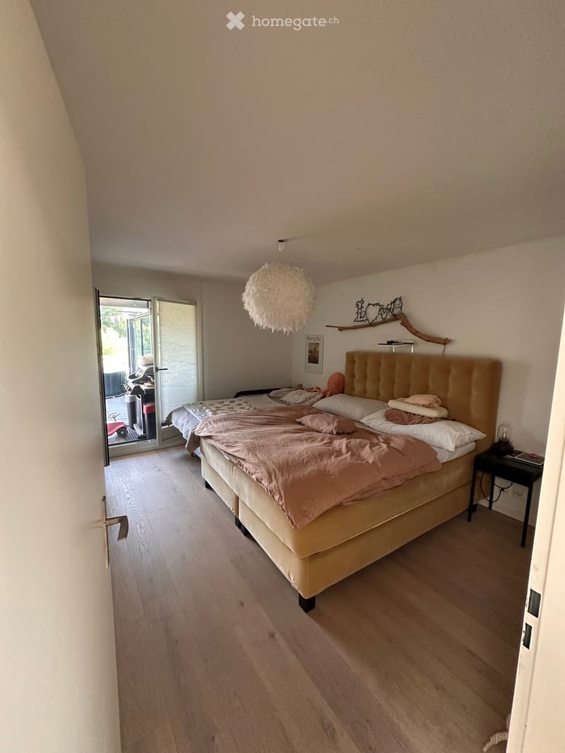 Cozy bedroom with a large bed, beige bedding, wooden floor, and a hanging spherical light fixture.