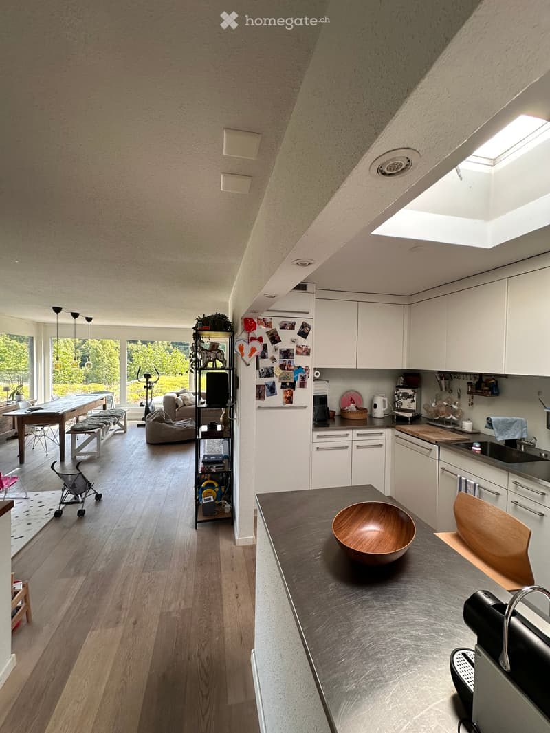 Open-plan kitchen and living area with white cabinets, wooden floor, island counter, and a sofa in the background.