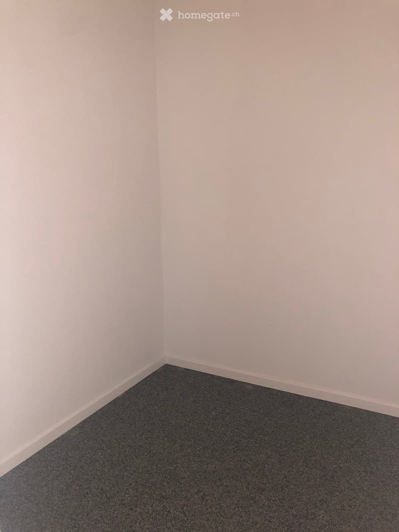 Empty room with white walls and grey carpeted floor, no furniture or equipment visible.