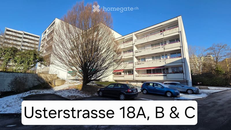 Multi-story apartment building with balconies, surrounded by trees and parked cars in a snowy parking lot.