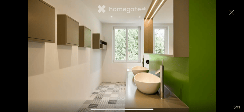 Modern bathroom with two white sinks, sleek faucets, built-in cabinets, and large windows offering a view of greenery.