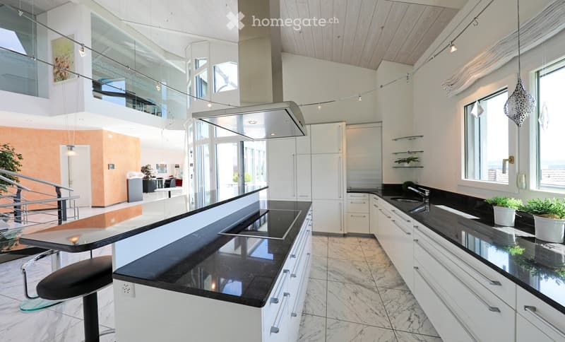 Modern kitchen with white cabinets, black countertops, and a central island with a built-in sink and stove. Features a sleek design with pendant lighting and a view of an adjacent living area.