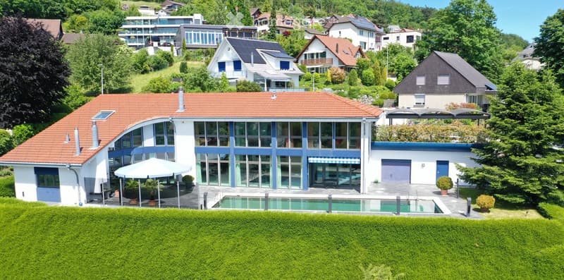A modern two-story house with a red-tiled roof, large windows, and a swimming pool in the front yard. The house features a garage and is surrounded by lush greenery and neighboring houses.