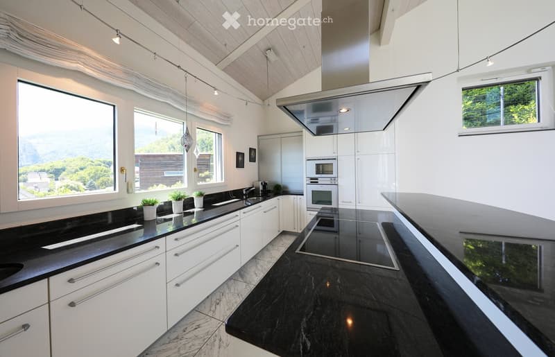 Modern kitchen with white cabinets, black countertops, stainless steel appliances, and large windows offering a scenic view.