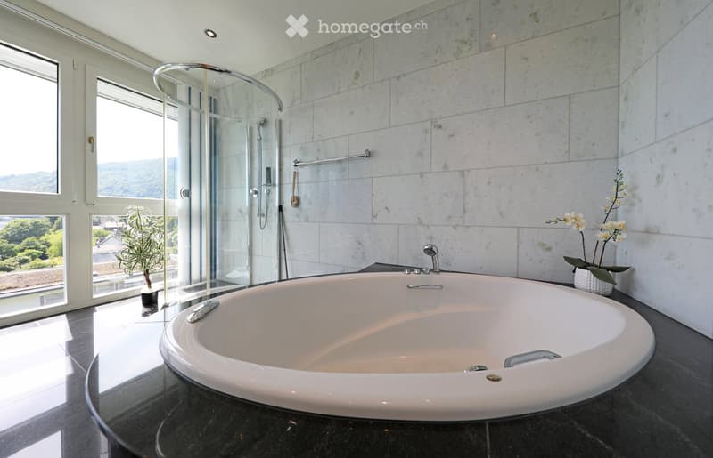 Modern bathroom with a large, freestanding bathtub, glass-enclosed shower, marble tiles, and a scenic view through large windows.