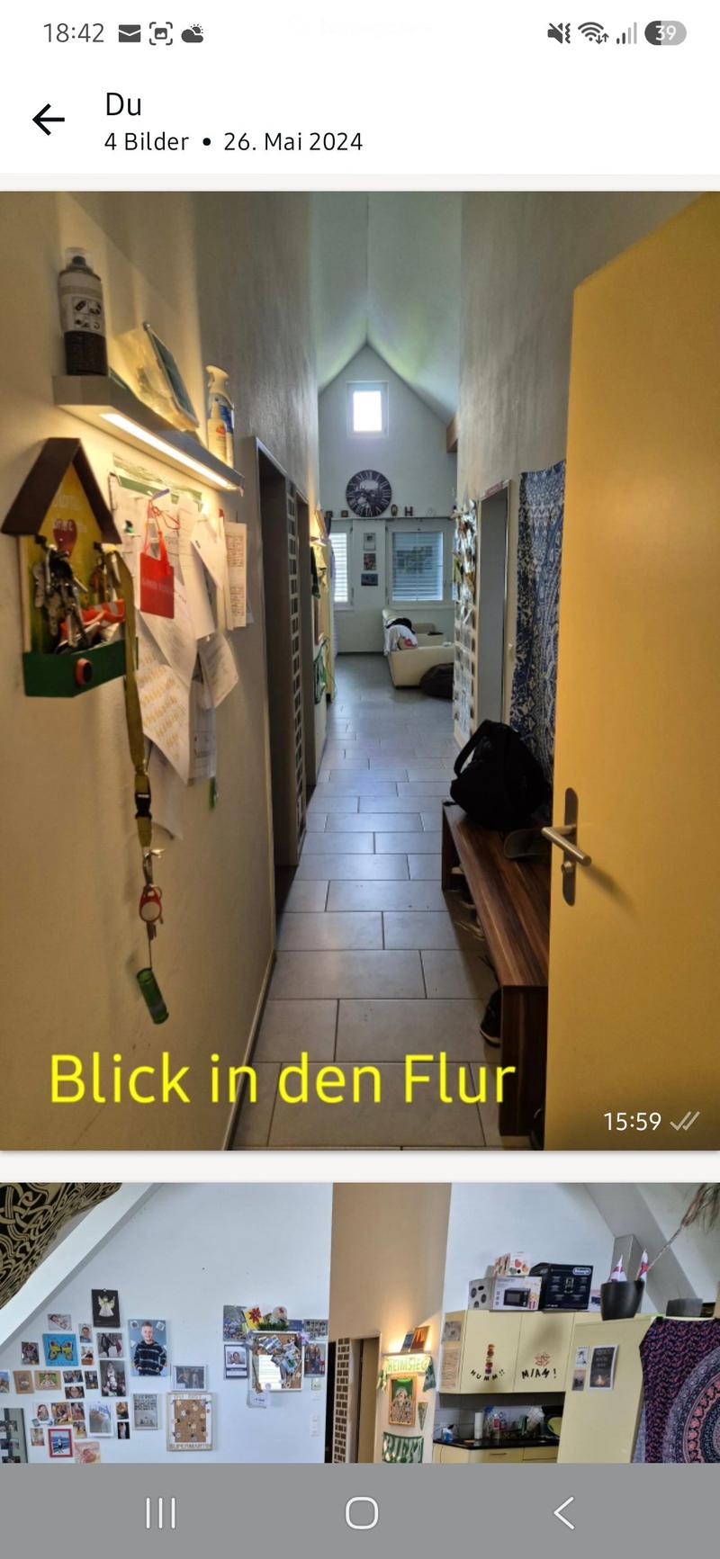 A narrow hallway with a slanted ceiling, white tiled floor, and a small window at the far end. The walls are adorned with various items, including a clock, a shelf with cleaning supplies, and a small table with a bag on it.