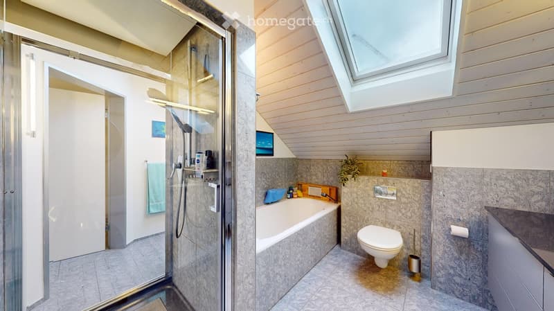 Modern bathroom with a bathtub, toilet, glass-enclosed shower, and built-in cabinets. Features a skylight window and marble-style tiles.