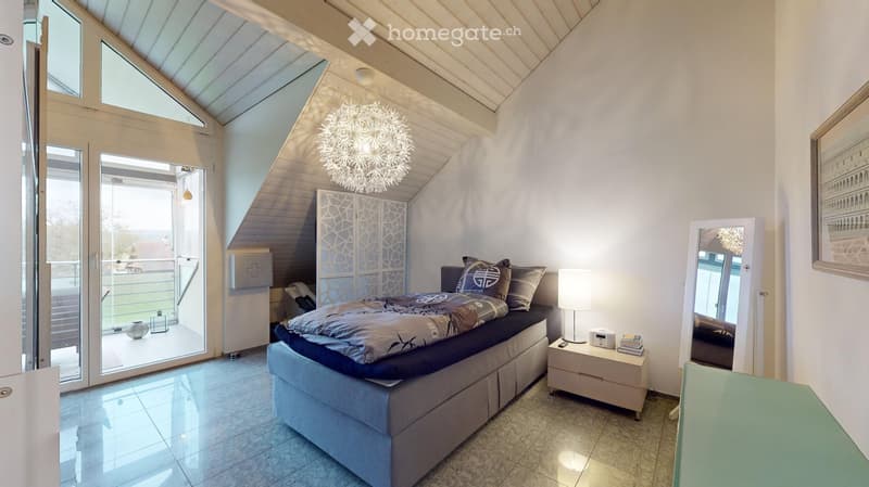 Modern bedroom with a large bed, nightstand, lamp, mirror, and a stylish chandelier. The room features large windows and a sliding door leading to a balcony.