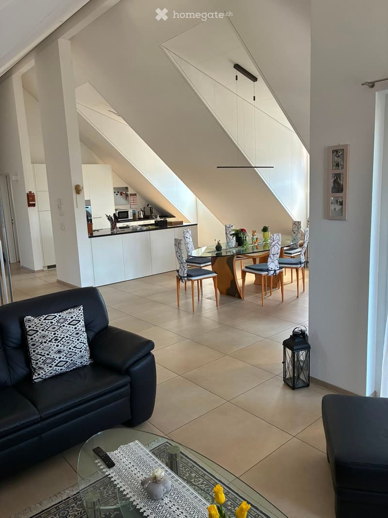 Modern living and dining area with a black leather sofa, glass coffee table, dining table with chairs, kitchen area, and decorative items.