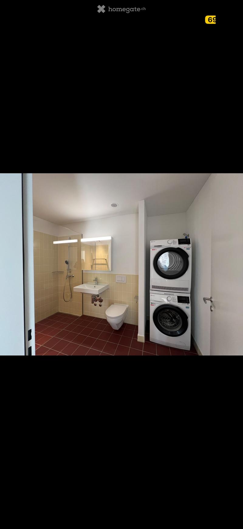 Modern bathroom with a sink, toilet, mirror, shower, and a stacked washing machine and dryer unit.