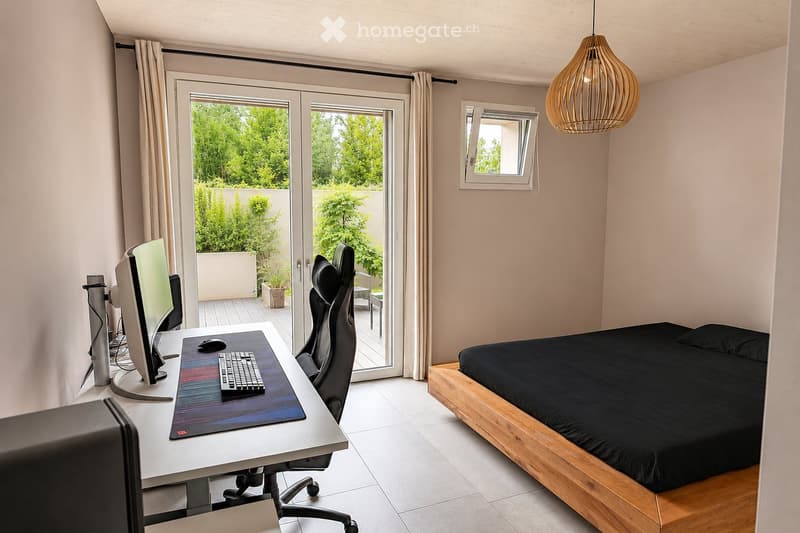 Modern bedroom with a wooden bed frame, desk with computer setup, and large window with balcony access.