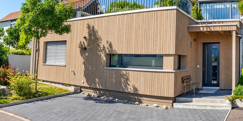 Modern two-story house with wooden siding, large windows, balcony, and small garden area.