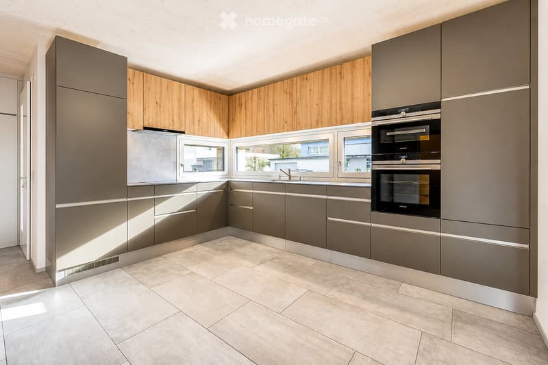 Modern kitchen with grey and wooden cabinets, stainless steel appliances, and large windows letting in natural light.