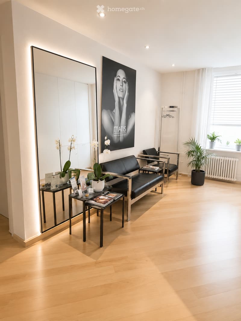 Modern, minimalist room with light wooden flooring, a black leather sofa, a matching chair, small side tables, a large mirror, and a large artwork on the wall.