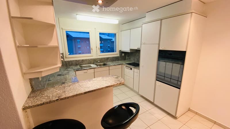 Modern kitchen with white cabinets, granite countertop, sink, oven, and two black stools.