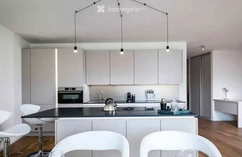 Modern kitchen with white cabinets, black countertop, and pendant lights. Includes an oven, sink, teapot, and stools.