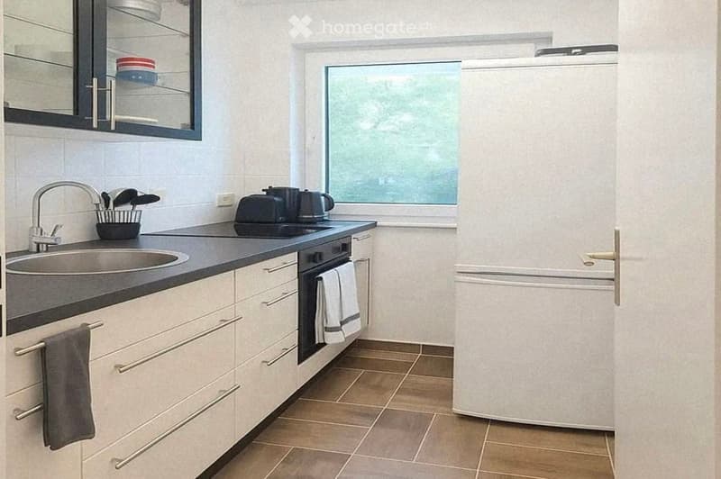 Modern kitchen with white cabinets, stainless steel sink, refrigerator, oven, and various kitchen utensils.